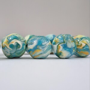 May include: A collection of colorful marbles with a swirled pattern. The marbles feature shades of blue, yellow, and white, creating a marbled effect. The marbles are round and appear to be made of glass or a similar material.