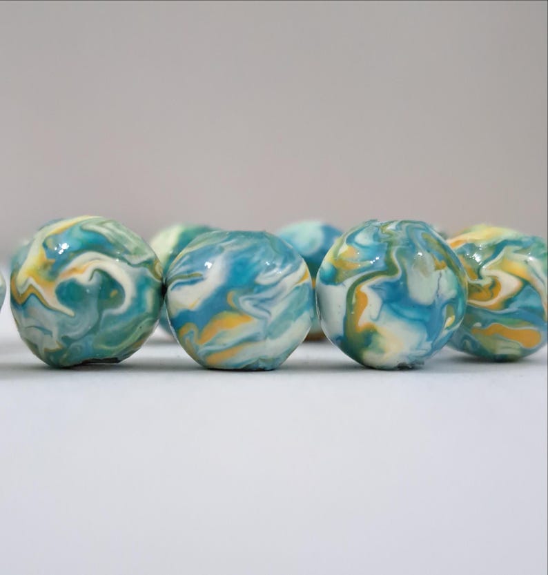 May include: A collection of colorful marbles with a swirled pattern. The marbles feature shades of blue, yellow, and white, creating a marbled effect. The marbles are round and appear to be made of glass or a similar material.
