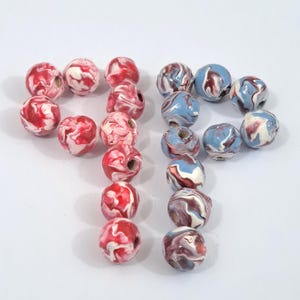 May include: A collection of round beads in two color schemes. One set features red and white marbled patterns, while the other showcases blue, white, and burgundy swirls. These beads are ideal for jewelry making and crafting projects.