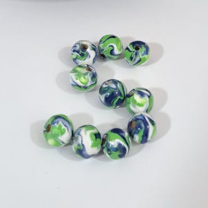 May include: A collection of round beads with a marbled design. The beads feature swirls of white, green, and navy blue. Each bead has a small hole for stringing. These beads are suitable for jewelry making and craft projects.