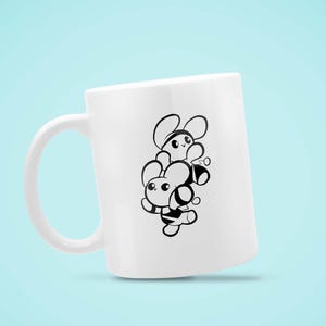 May include: White ceramic mug featuring a black and white cartoon design of two bees stacked on top of each other. The bees have large eyes and are smiling. The mug has a curved handle and is set against a light blue background.