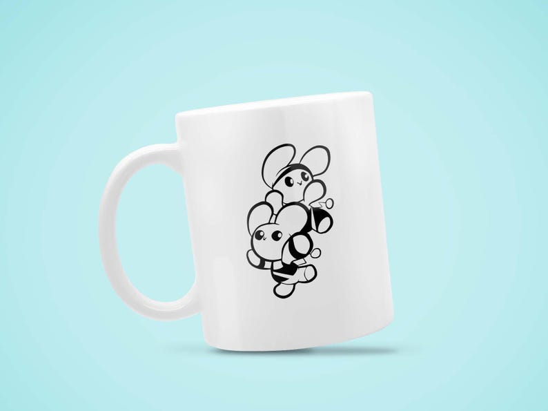 May include: White ceramic mug featuring a black and white cartoon design of two bees stacked on top of each other. The bees have large eyes and are smiling. The mug has a curved handle and is set against a light blue background.