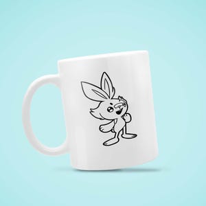 May include: White ceramic mug featuring a black and white cartoon rabbit illustration. The rabbit has large ears and is smiling. The mug has a curved handle and is set against a light blue background.