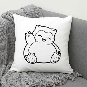 May include: White square pillow featuring a black and white cartoon illustration of a Snorlax character. The Snorlax is waving with a happy expression. The pillow is on a gray couch with a gray knitted throw blanket.