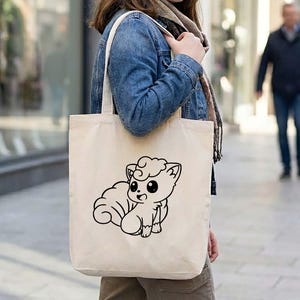 May include: A beige tote bag featuring a black and white cartoon cat illustration. The cat has large eyes and a fluffy tail. The bag is carried by a person walking on a city street.