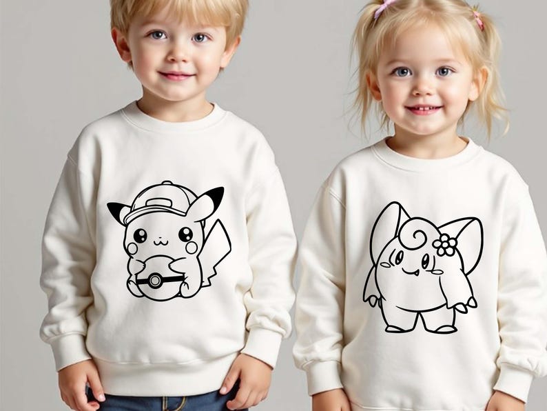 May include: Two off-white sweatshirts featuring black line art of Pok&eacute;mon characters. One sweatshirt has Pikachu wearing a cap and holding a Pok&eacute; Ball. The other has a Clefairy design. Both are long-sleeved.