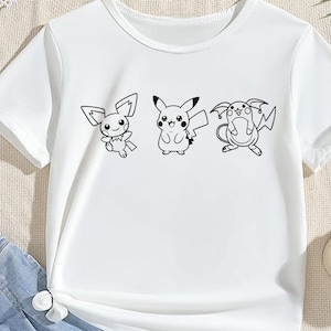May include: White t-shirt featuring three black and white cartoon characters. The characters are Pikachu and two other Pokemon. The shirt has a crew neck and short sleeves. The design is centered on the front of the shirt.