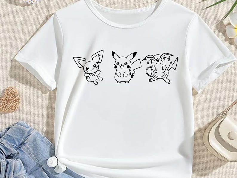 May include: White t-shirt featuring three black and white cartoon characters. The characters are Pikachu and two other Pokemon. The shirt has a crew neck and short sleeves. The design is centered on the front of the shirt.