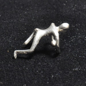 May include: A silver-toned abstract sculpture of a person in a crouching pose.