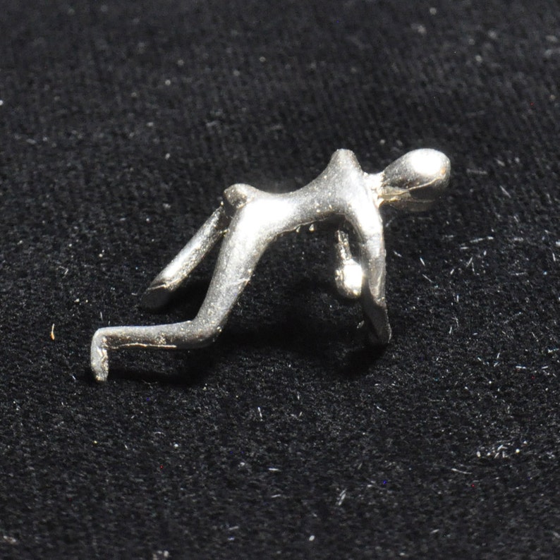 May include: A silver-toned abstract sculpture of a person in a crouching pose.
