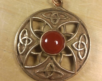 May include: A round, gold-toned pendant with a Celtic knot design and a red carnelian stone in the center.
