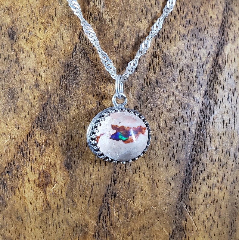 May include: A silver chain necklace with an oval-shaped pendant featuring a white opal with iridescent green and blue flashes. The pendant is set in a silver bezel with a decorative border.