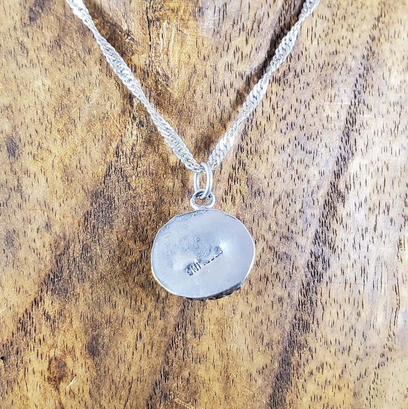 May include: Silver necklace with a round pendant. The back of the pendant has the inscription "925 STERLING".