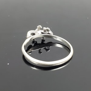May include: A silver ring with a detailed design of two figures holding hands. The ring is simple and elegant.