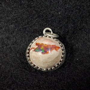 May include: A silver pendant with a round, white opal stone with iridescent flashes of red, green, and blue. The opal is set in a silver bezel with a beaded edge.