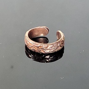 May include: A gold-toned ear cuff with a detailed floral design. The cuff is open and has a slight bend to fit comfortably on the ear.