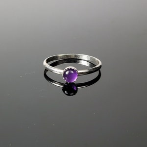 May include: A silver ring with a small, round, purple amethyst gemstone.