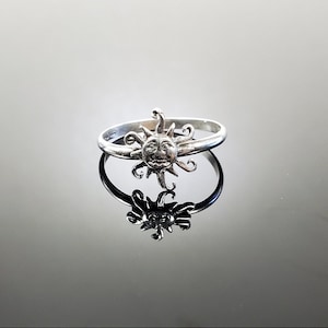 May include: A silver ring with a sun design. The sun has a face and rays.
