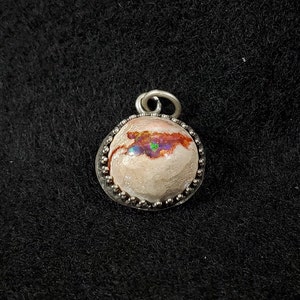 May include: A silver pendant with a round opal stone set in a beaded bezel. The opal has a white base with iridescent flashes of pink, green, and blue.