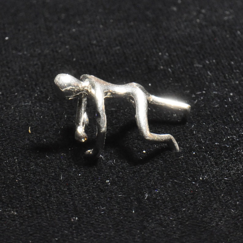May include: Silver abstract sculpture of a person in a bent-over pose. The sculpture is made of smooth, shiny metal and has a modern, minimalist design.