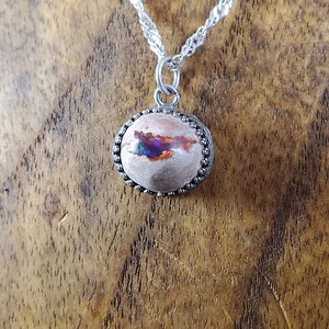 May include: A silver chain necklace with a round pendant featuring a pink and white opal with iridescent blue and purple flashes. The pendant is set in a silver bezel with a beaded edge.
