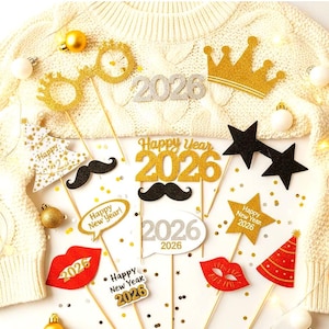 Può includere: Una collezione di oggetti di scena per fototessere di Capodanno, tra cui occhiali glitterati dorati, corone, baffi, labbra, stelle e fumetti. Gli oggetti di scena presentano l'anno 2026 e il testo "Happy New Year!" su un maglione color crema.