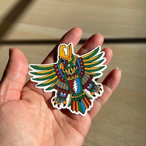 May include: A colorful sticker of a stylized eagle with green, yellow, red, and blue details. The eagle has a large, detailed head and wings spread out.