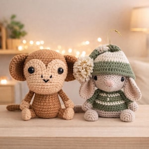 Puede incluir: Dos animales de peluche de ganchillo hechos a mano: un mono marrón y un conejito con un gorro y un suéter a rayas verdes y blancas. El mono tiene orejas grandes y una cara sonriente. El conejito tiene orejas largas y un pompón en su gorro. Están sobre una superficie de madera.