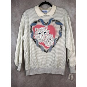 May include: A light grey striped sweatshirt with a cream collar. It features a pink heart design with two white cat faces and blue ribbon details. The brand name "Karen Blake" is visible on the collar.