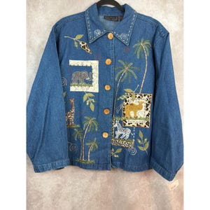 May include: Blue denim jacket with embroidered safari animal and palm tree designs. Features an elephant, giraffe, zebra, and camel. The jacket has wooden buttons and a collar with embroidered details.