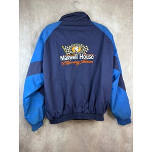 May include: Navy blue and light blue Maxwell House Racing Team jacket. The jacket has a full zip, a stand-up collar, and elastic cuffs and hem. The Maxwell House Racing Team logo is on the back of the jacket.