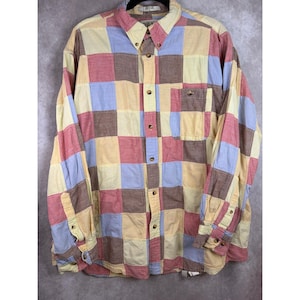 May include: A long-sleeve button-down shirt featuring a multi-colored patchwork pattern of squares in shades of light blue, yellow, red, and brown. The shirt includes a pointed collar, a single chest pocket on the left side, and buttoned cuffs.