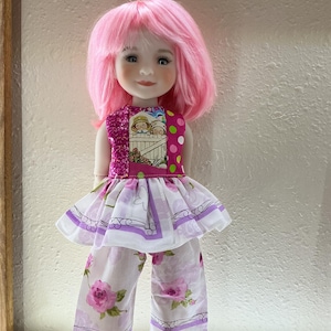 May include: A doll with pink hair and a matching outfit. The doll's top is a patchwork of pink and patterned fabrics, and the skirt and pants feature a floral print. The doll is wearing pink shoes.