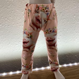 Puede incluir: Leggins rosas con un patrón de cerdos sonrientes que llevan coronas de flores.