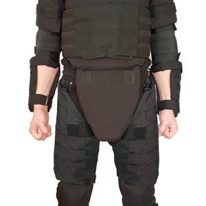 May include: Black tactical body armor set, including a vest, shoulder pads, arm guards, groin protector, and leg guards. The set is designed for protection and features multiple straps and panels. The person is wearing black combat boots.