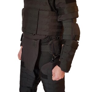 May include: Black tactical body armor set, including a vest, arm and leg protection. The set features multiple pockets and adjustable straps. The person in the image is wearing black boots.