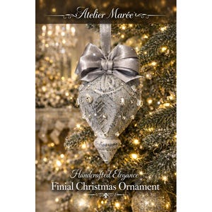 May include: A silver finial Christmas ornament with a large bow and sparkling embellishments. The ornament is hanging on a Christmas tree with lights. The text "Atelier Maree" and "Handcrafted Elegance Finial Christmas Ornament" are visible.