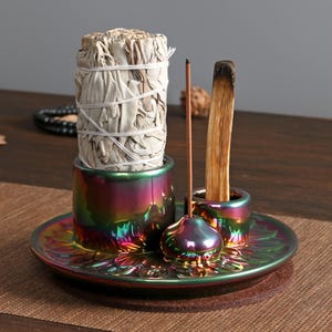 Può includere: Un porta incenso in ceramica iridescente multicolore con un fascio di salvia bianca, un bastoncino di incenso e un pezzo di palo santo. Il supporto ha una base rotonda e tre scomparti separati.