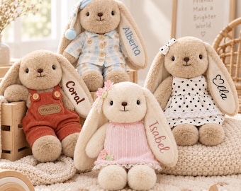 May include: Four plush bunny toys with long ears, each wearing different outfits. One wears blue plaid pyjamas, one wears rust-coloured overalls, one wears a pink dress, and one wears a white polka-dot dress. Each bunny has a name embroidered on its ear.