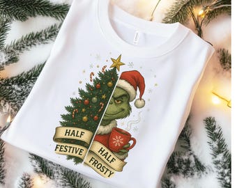 May include: White sweatshirt featuring a split design with a Christmas tree and the Grinch. The Grinch is wearing a Santa hat and holding a mug. The text reads "Half Festive Half Frosty".