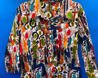 May include: A button-down jacket with a vibrant, abstract pattern. The jacket features a white base with colorful shapes in red, orange, blue, green, and yellow. It has long sleeves and two chest pockets. The jacket is hanging on a black hanger.