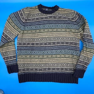 Puede incluir: Un suéter de manga larga con un diseño estampado en tonos de azul, verde, gris y beige. El suéter tiene cuello redondo y puños acanalados. El logo de GAP es visible en la parte posterior del cuello.