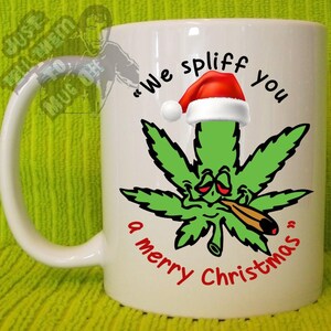 Puede incluir: Taza de cerámica blanca con una hoja de cannabis con un gorro de Papá Noel y fumando un cigarrillo. La taza tiene el texto "We spliff you a merry Christmas" en negro y rojo.