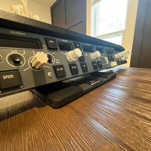 May include: A dark gray flight simulator mode control panel featuring white knobs, black push buttons, and digital display windows. The panel includes labels such as IAS/MACH, SPEED, and LVL CHG, with a small Boeing logo visible on the black base stand.