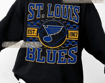May include: Black sweatshirt featuring the text "ST. LOUIS BLUES" in blue and gold lettering. The design includes a logo with a musical note and wings, and the year "1967". The sweatshirt is a classic style.
