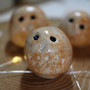 May include: Three small, round, ceramic owl figurines with a glossy, speckled beige and tan glaze. Each owl features two dark, circular eyes, a small pointed beak, and carved feather details on the chest, arranged in a cluster.