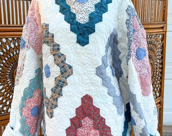 May include: A long-sleeved quilted pullover featuring a patchwork design of hexagonal fabric pieces in various patterns and colors, including red, blue, teal, and white. The garment has a round neckline and white cuffs on the sleeves.
