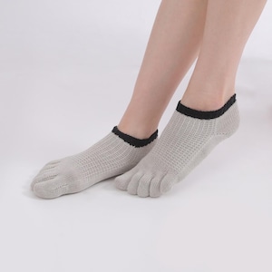Puede incluir: Calcetines de color gris claro con ribetes negros en los tobillos. Los calcetines tienen una textura similar a la malla y están diseñados para separar cada dedo del pie.