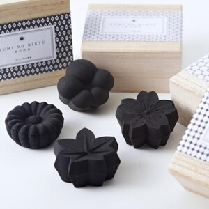 以下が含まれることがあります： 様々な花の形や雲の形をした黒い装飾用の炭のコレクション。炭の作品は、日本のテキストと装飾的な模様が入った木箱と一緒に展示されています。これらのアイテムは、インテリア装飾用です。