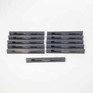 以下が含まれることがあります： グレーのパッケージに入った、チャコール歯ブラシのコレクション。各パッケージには日本語のテキストとミニマルなデザインが施されています。歯ブラシは白い表面にきれいに配置されています。